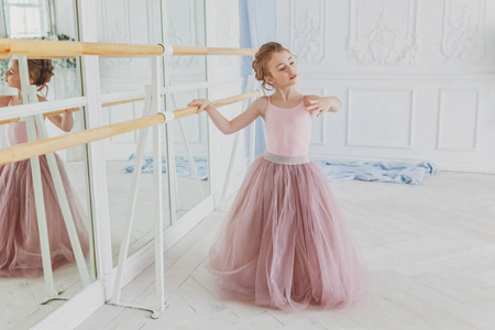 舞蹈课上的年轻古典芭蕾舞演员。 在白色的光厅里，穿着粉红色的芭蕾舞裙，靠近大镜子