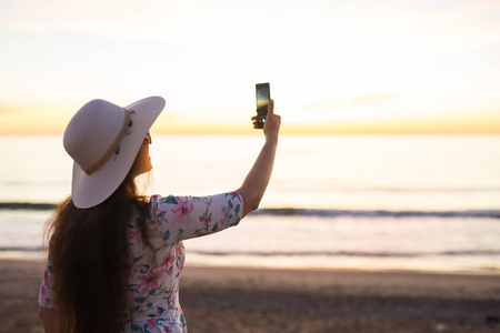 技术旅行和假期概念年轻女子在海上智能手机日出时拍照