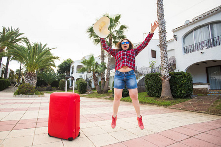 旅行旅游情绪和人的概念快乐的年轻女子在红色的行李箱附近跳着帽子, 戴着阳光明媚的眼镜