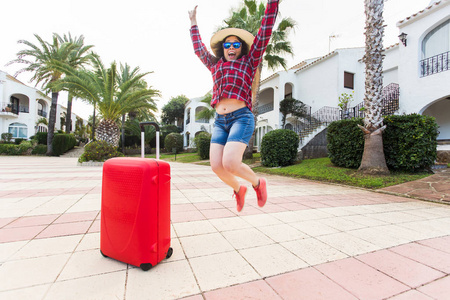 旅行, 旅游, 情绪和人的概念快乐的年轻女子有乐趣在她的红色手提箱附近的帽子和阳光明媚的眼镜鬼混