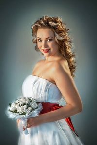 年轻的新娘穿着白色连衣裙，带着一束鲜花，在灰色的背景上显示出美丽的婚礼发型
