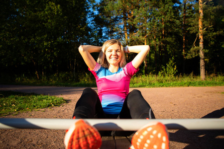 快乐的金发碧眼的妇女在公园的木长凳上练习在夏天
