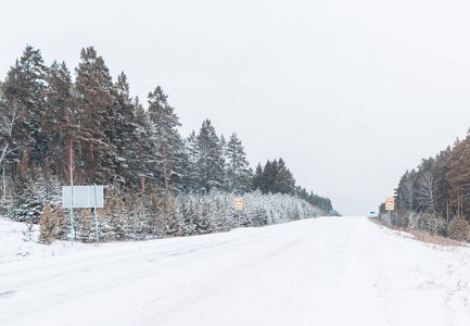 风景明信片风景林。 冬天的美丽景色。 冬天雪覆盖的道路雪道标志。