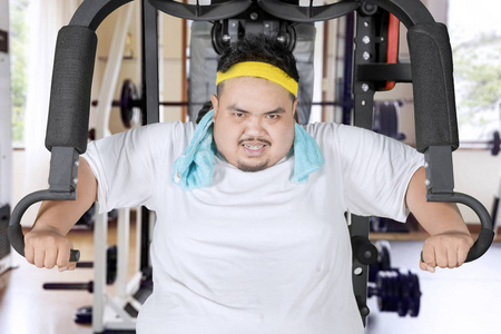 在健身中心用健身机锻炼的年轻胖子形象照片