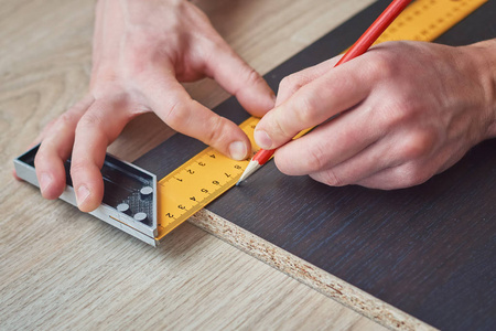 男性用尺子和铅笔测量木板的手照片