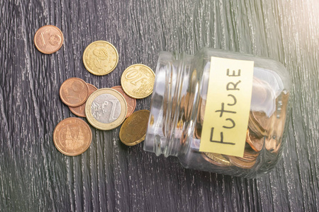打开倾斜的玻璃罐与分散的欧元硬币与铭文未来在一个黑色的木制桌子。 预期节省的概念