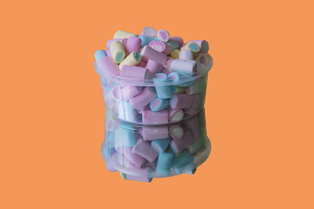 彩色棉花糖糖果在塑料容器和镜子上的橙色背景。