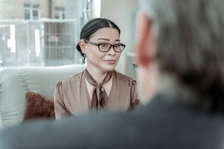 黑头发优雅的女人在棕色缎子衬衫看起来惊讶