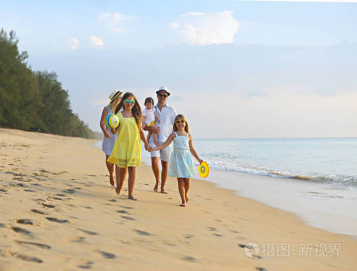 快乐的年轻家庭在海滩上玩得开心，在日落时跑步和跳跃