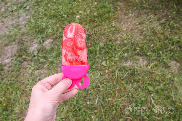 在温暖的阳光明媚的日子里，手拿草莓冰淇淋锥在夏天的自然背景上。 自制新鲜水果甜点。