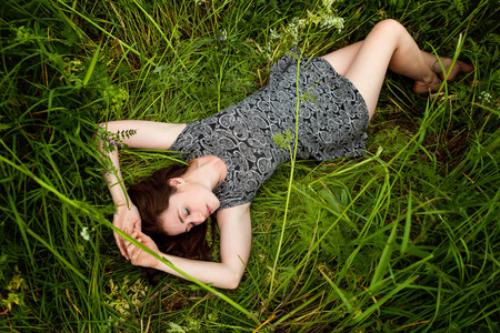 黑发女人躺在绿草上。 美丽的女孩在户外享受自然和放松。 自由快乐的女人。 顶部视图