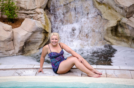 一个金发女人穿着两件比基尼，在一个豪华度假胜地的室外游泳池里摆姿势
