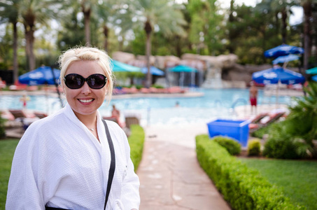 在一个豪华度假胜地的室外泳池区，身穿白色水疗浴袍的金发女子