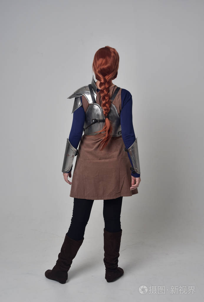 一个穿着中世纪战士服装和钢甲的红头发女孩的全长肖像,站着的姿势,背