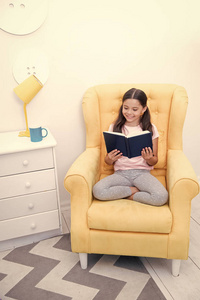 读书是她的爱好。女孩坐在黄色扶手椅上看书。孩子准备上床睡觉。在舒适的卧室愉快的时间。女孩长头发可爱的睡衣放松和阅读童话书睡前