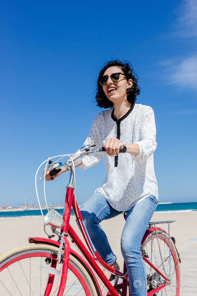 微笑的年轻女子骑自行车在海滩上