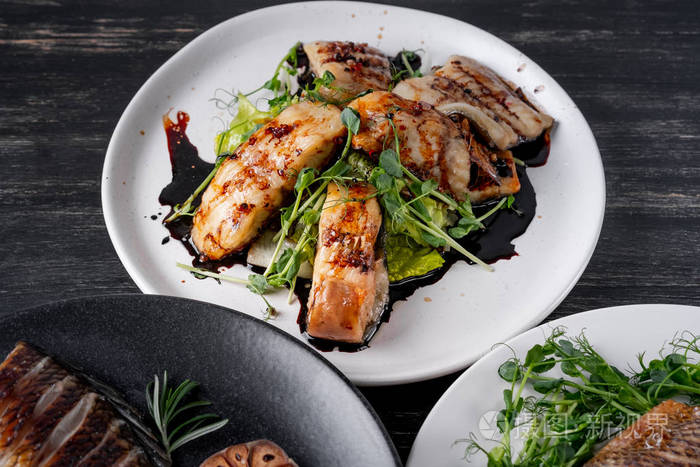 各种烤鱼菜肴在白色和黑色盘子上配上绿色沙拉