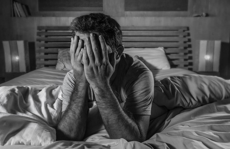 躺在床上的年轻迷人悲伤和沮丧的男人的戏剧性肖像，感到焦虑抑郁焦虑危机体贴和沉思，晚上睡在家里的卧室里。