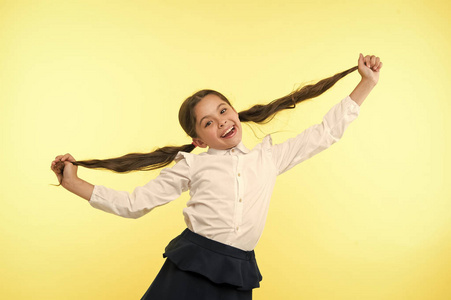 快乐的女孩在黄色背景上显示长黑发。小孩用新发型微笑。美发沙龙服务。为她美丽的头发骄傲。美容院。时尚和可爱