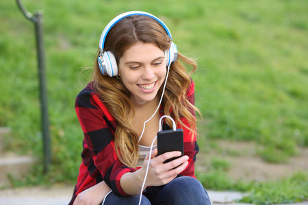 快乐的青少年听音乐检查智能手机坐在公园里