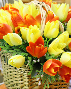 前景中的春花。 一束人造郁金香站在柳条篮子里。 郁金香是黄色和橙色的。