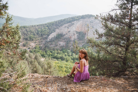 那个女孩坐在岩石上。 沿着河跑。 在岩石和树冠后面