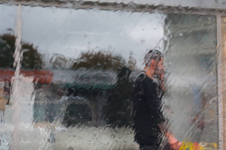 雨滴在汽车玻璃上，焦点在雨滴上。 看着街道，一个男人在打电话