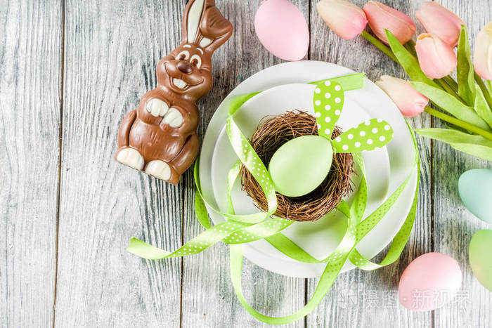 复活节节日桌上摆满了兔子和鸡蛋，盘子里放着五颜六色的鸡蛋和巧克力兔子，节日彩带，木制背景，俯视着复制品