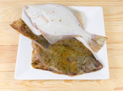 在一张木制的乡村餐桌上,在白色的方形盘子上放两条生的鱼摄影图