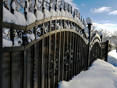 金属栅栏与锻造元素附近的房子冰柱上的雪和房子的冬天