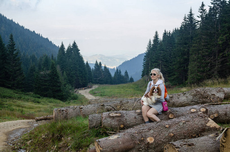 女徒步旅行者和她的狗在山上的一块木头上休息