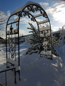 房子附近有锻造元素的金属拱门，雪背景上有冰柱，冬天有房子