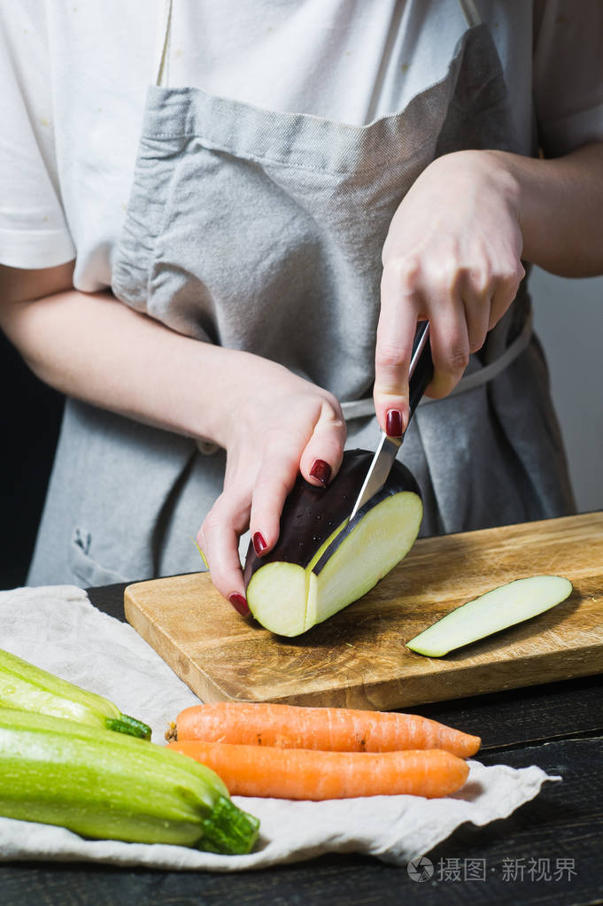 厨师的手把茄子切成木切割板侧视黑色背景关闭