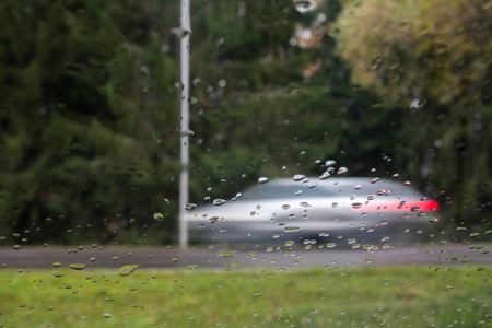 雨滴在汽车玻璃上，焦点在雨滴上。 观看街道和汽车的运动。 长曝光照片