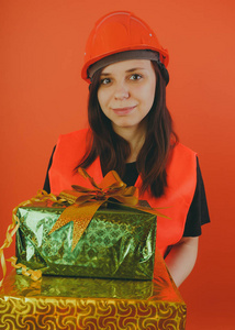 女孩建设者手中有礼物的概念，现金回馈礼品与购买或折扣。 一个戴着头盔穿着橙色背心的妇女，如装载机或建筑工人