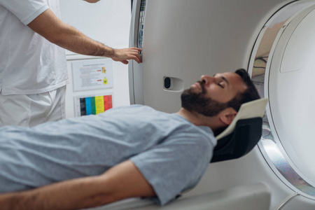 医疗技术人员按下ct扫描仪上的按钮，而他的病人躺在ct扫描仪床上。