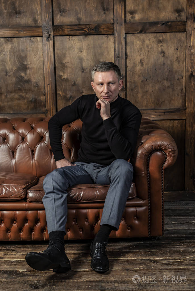 穿着黑色毛衣,坐在皮革沙发上的时髦优雅男人