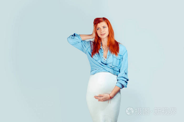 年轻的姜女怀孕的肚子手牵着头健忘地看着远离绝望孤立在浅蓝色的背景