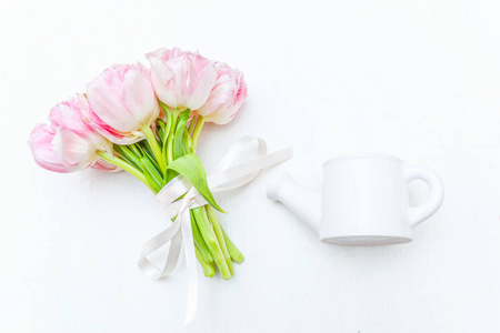 春天的贺卡。 一束清新的淡粉色郁金香花小玩具浇水罐花瓶白色背景。 节日快乐母亲节情人节概念。 平躺顶视复印空间
