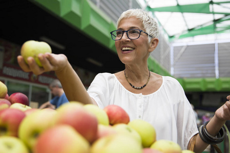 快乐的老妇人在市场上买苹果