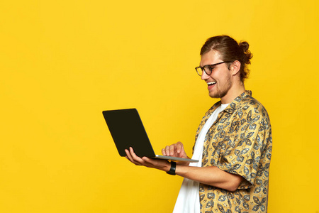 一个微笑的年轻人的肖像在眼镜使用笔记本电脑查出在橙色背景