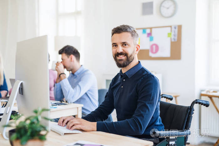 坐在轮椅上的年轻商人和在现代办公室工作的同事