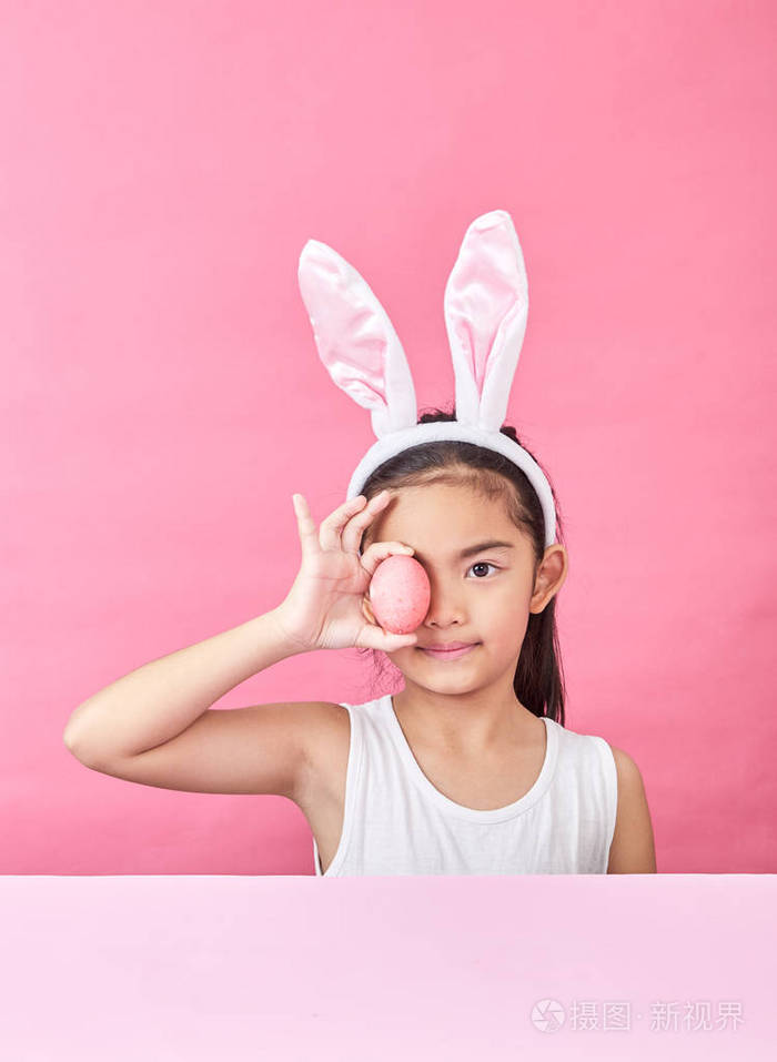 摄影棚拍摄一个快乐的小女孩戴着兔子耳朵,在粉红色的背景上举起一个