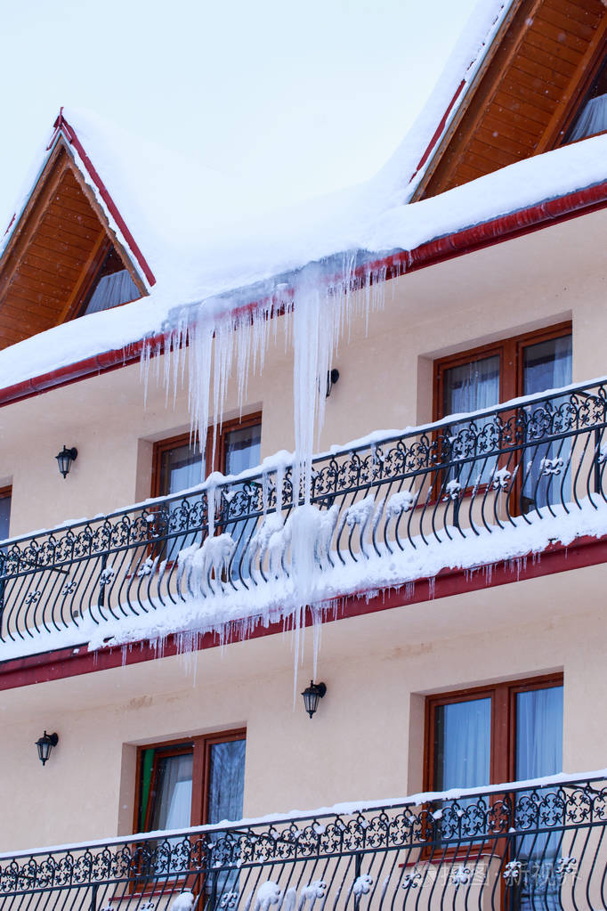尖锐的冰柱和融化的雪挂在屋顶的屋檐上