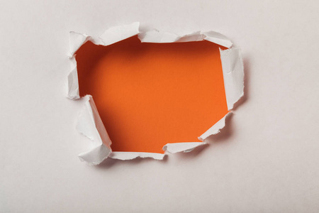 在橙色背景上的纸张上撕开的洞图片