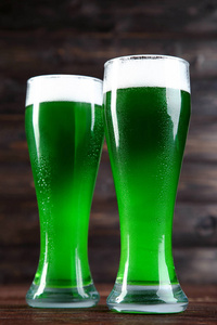 s Day. Glasses of green beer on wooden background