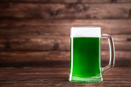 s Day. Glass mug with green beer on brown wooden background