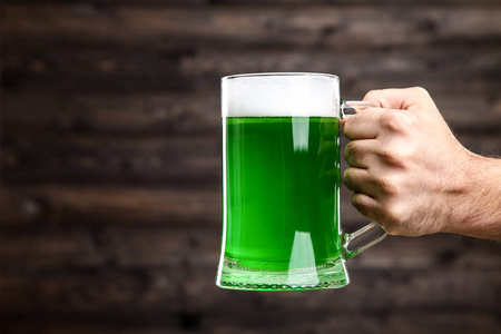 s Day. Glass mug with green beer in male hand on wooden backgrou