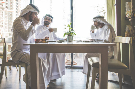 三个商人在迪拜喝茶，穿着传统的阿联酋服装