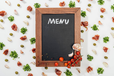 粉笔板的顶部视图，菜单字母在意大利火腿橄榄大蒜丁香和樱桃番茄中。
